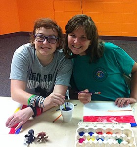 Noble employee and participant smiling while painting.