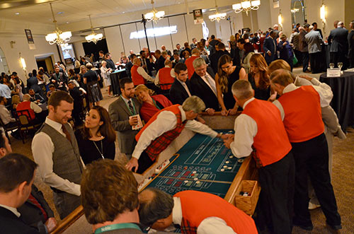 Large room of people playing various casino games at Raising the Stakes for Noble event.